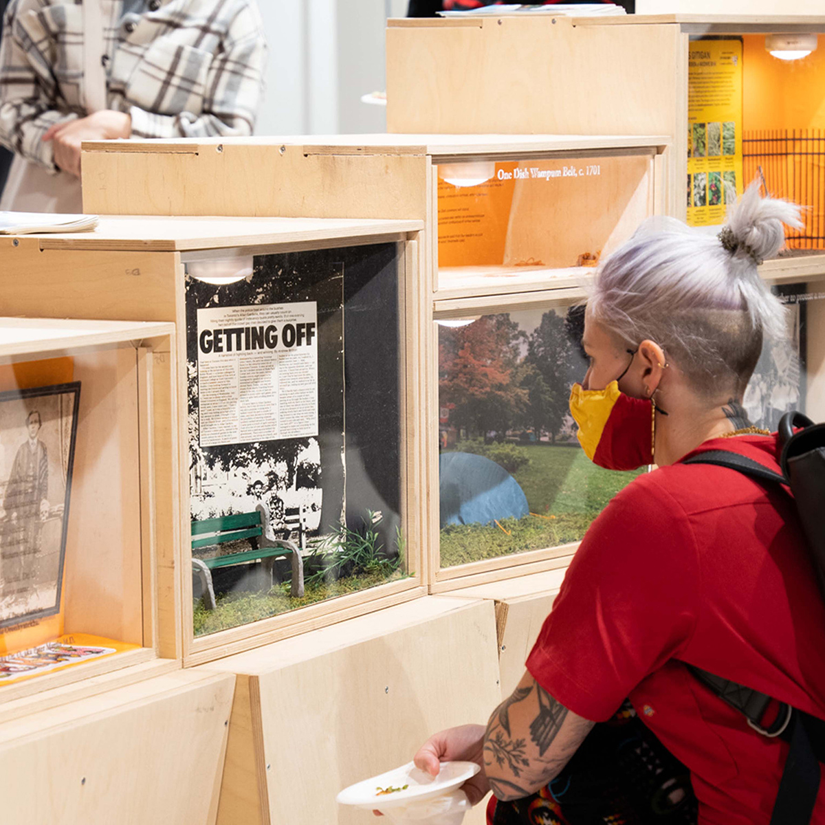 A guest with a mask crouches down to read a poster as part of the People, Power, and the Park exhibition at the Paul H. Cocker Gallery. 