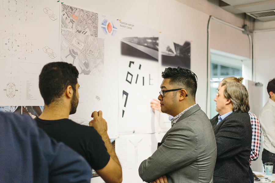 Two students speak in front of architectural drawings