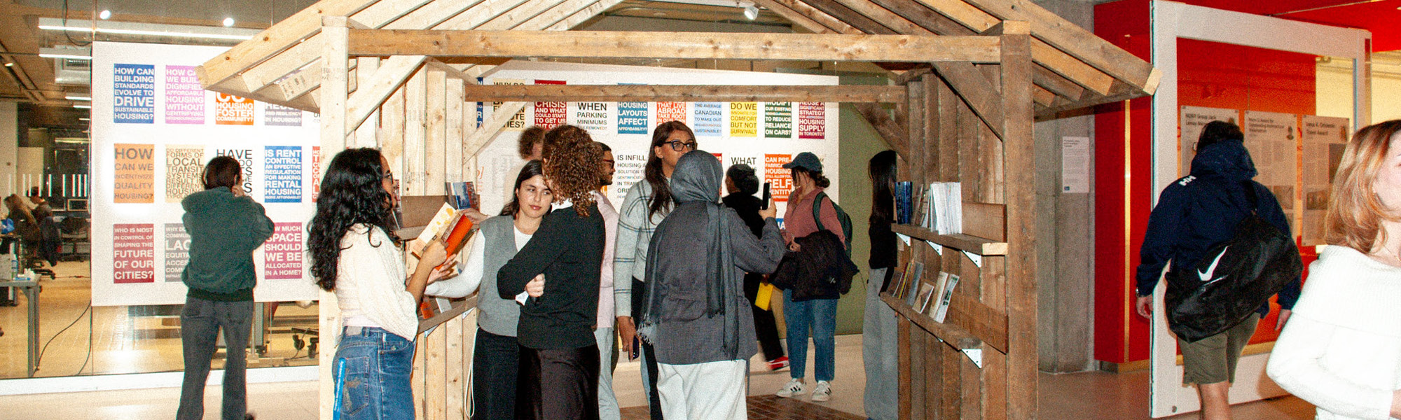 A group of students are exploring a zine exhibit. The zines are sitting on wood shelves in the shape of a house.