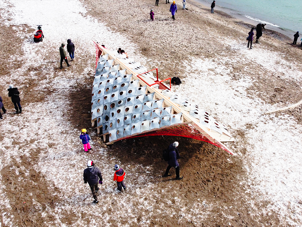 An aerial shot of the S'Winter pavilion on the beach. Children and visitors walk around the pavilion with snow on top of sand. 