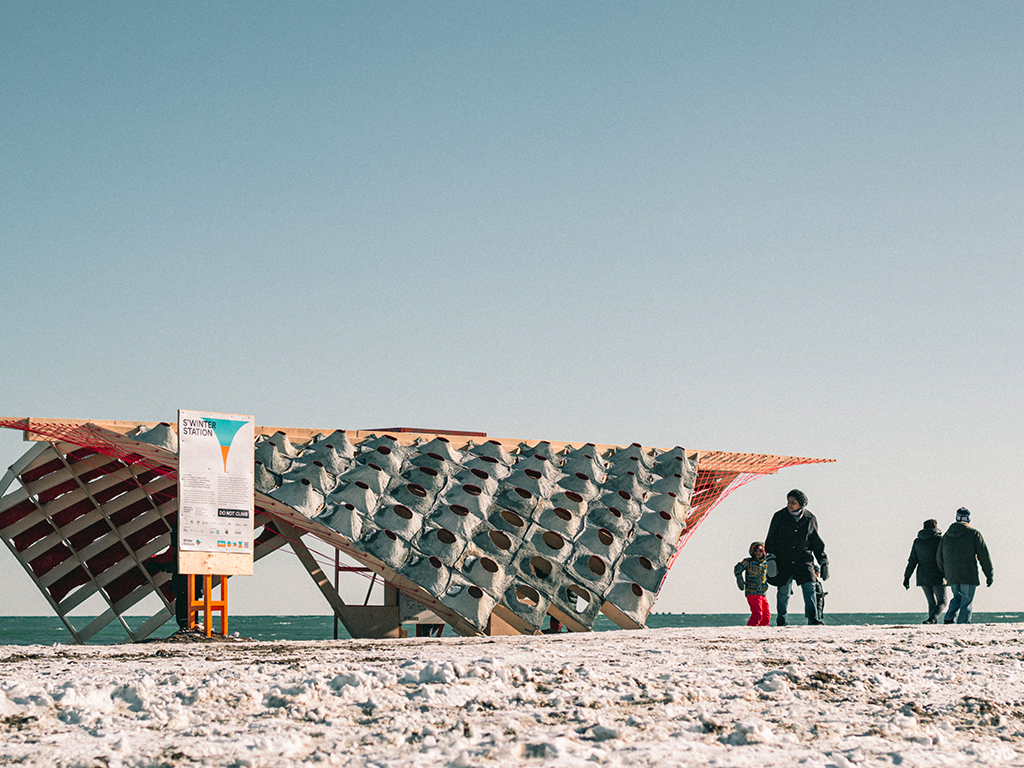 A wide-shot of the S'Winter pavilion by students on the beach. 