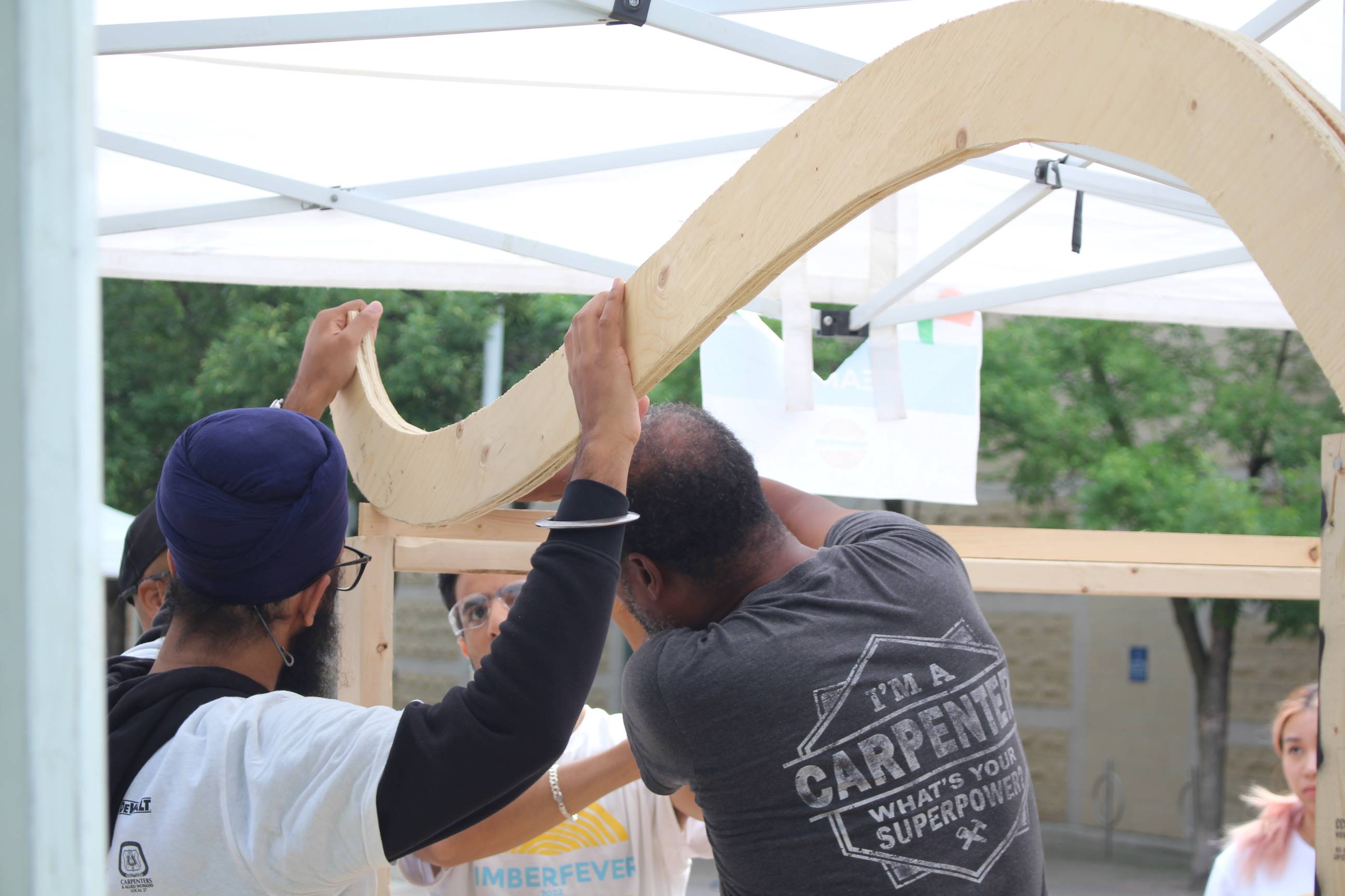 A mentor helps students attach a curved wooden piece. 