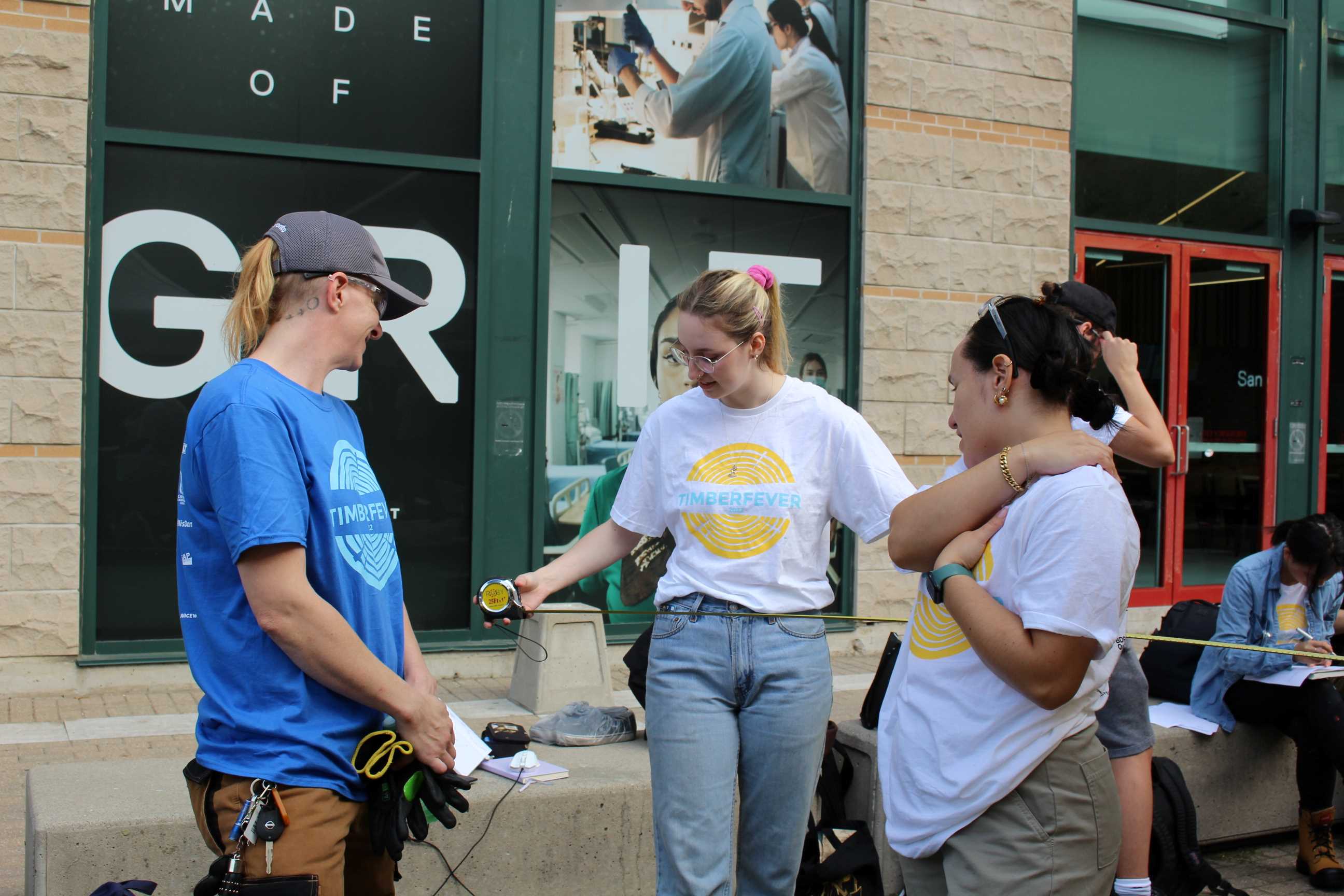 Student talking to a carpenter mentor while holding a measuring tape. 