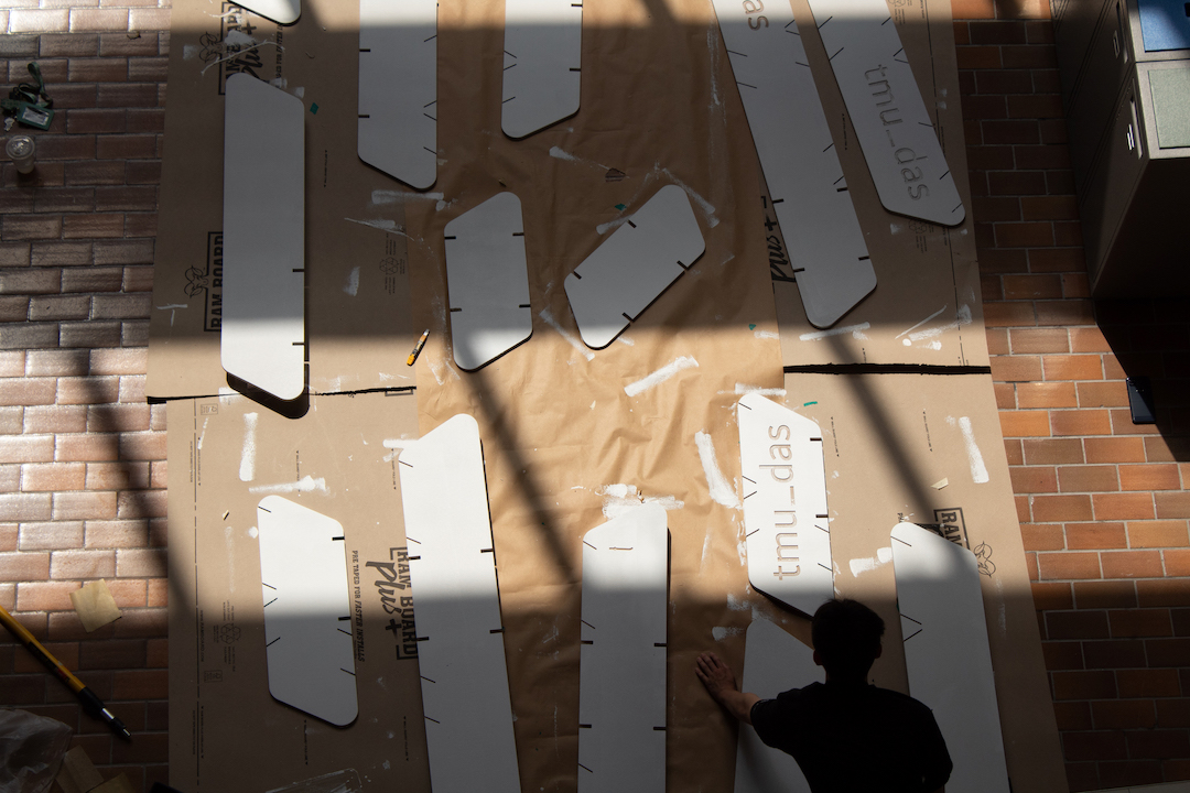An aerial shot overseeing students painting the wooden panels of the Cloud model white. 