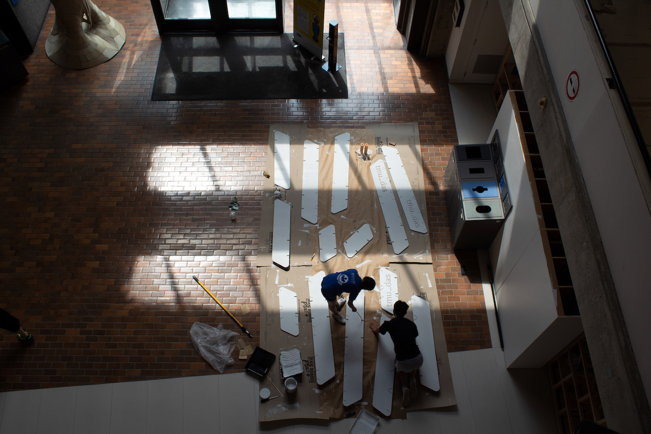 An aerial shot overseeing students painting the wooden panels of the Cloud model white. 