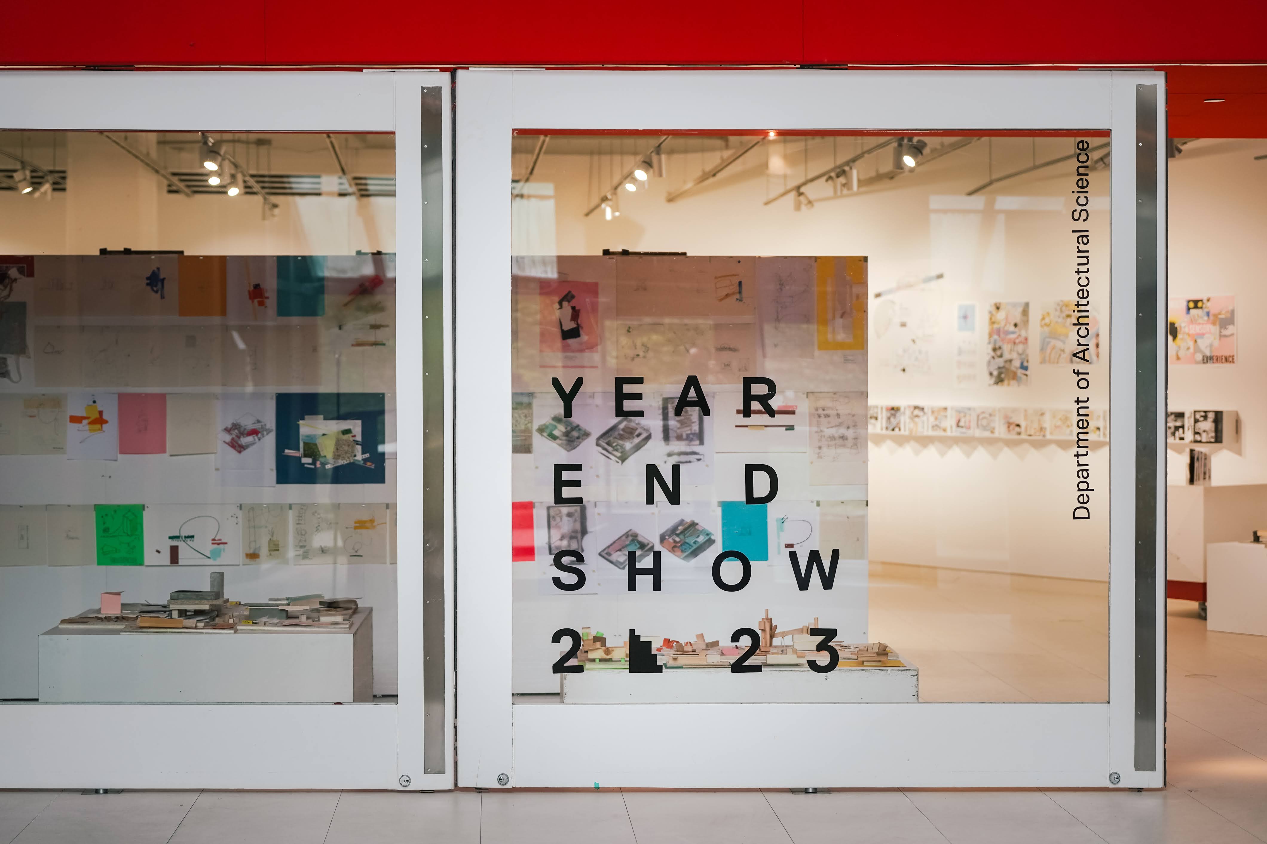 Glass window of the Paul H. Cocker Gallery which reads Year End Show 2023. Inside there is graduate architecture work. 