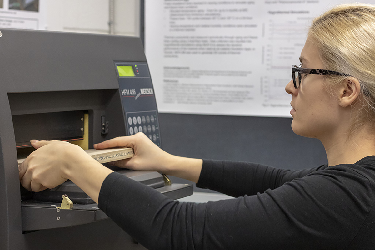 A student holds a block of building material inside a machine that tests thermal conductivity and thermal resistance. 