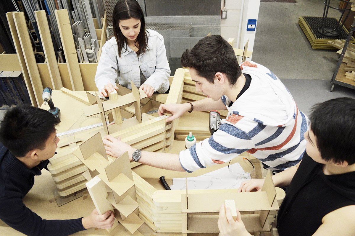 Four students glue together an architectural model made of wood.