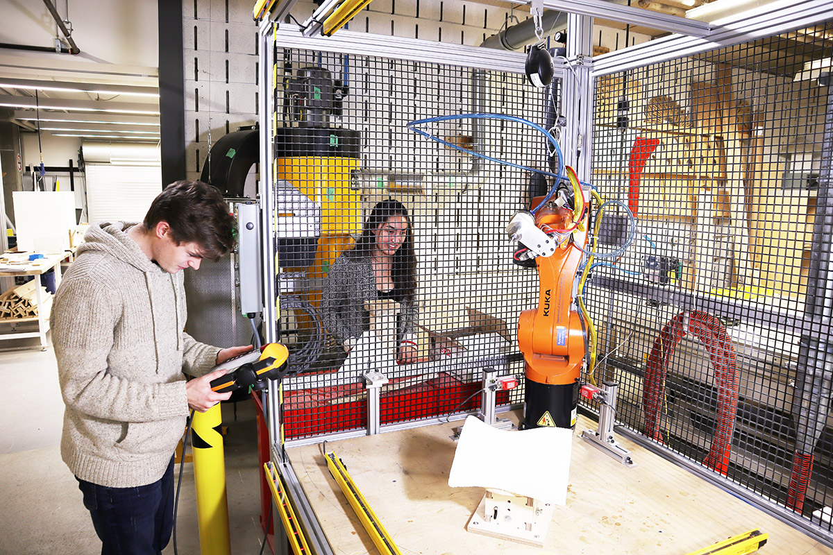 Two students operate a robotic arm located in the Robot and CNC Lab. 