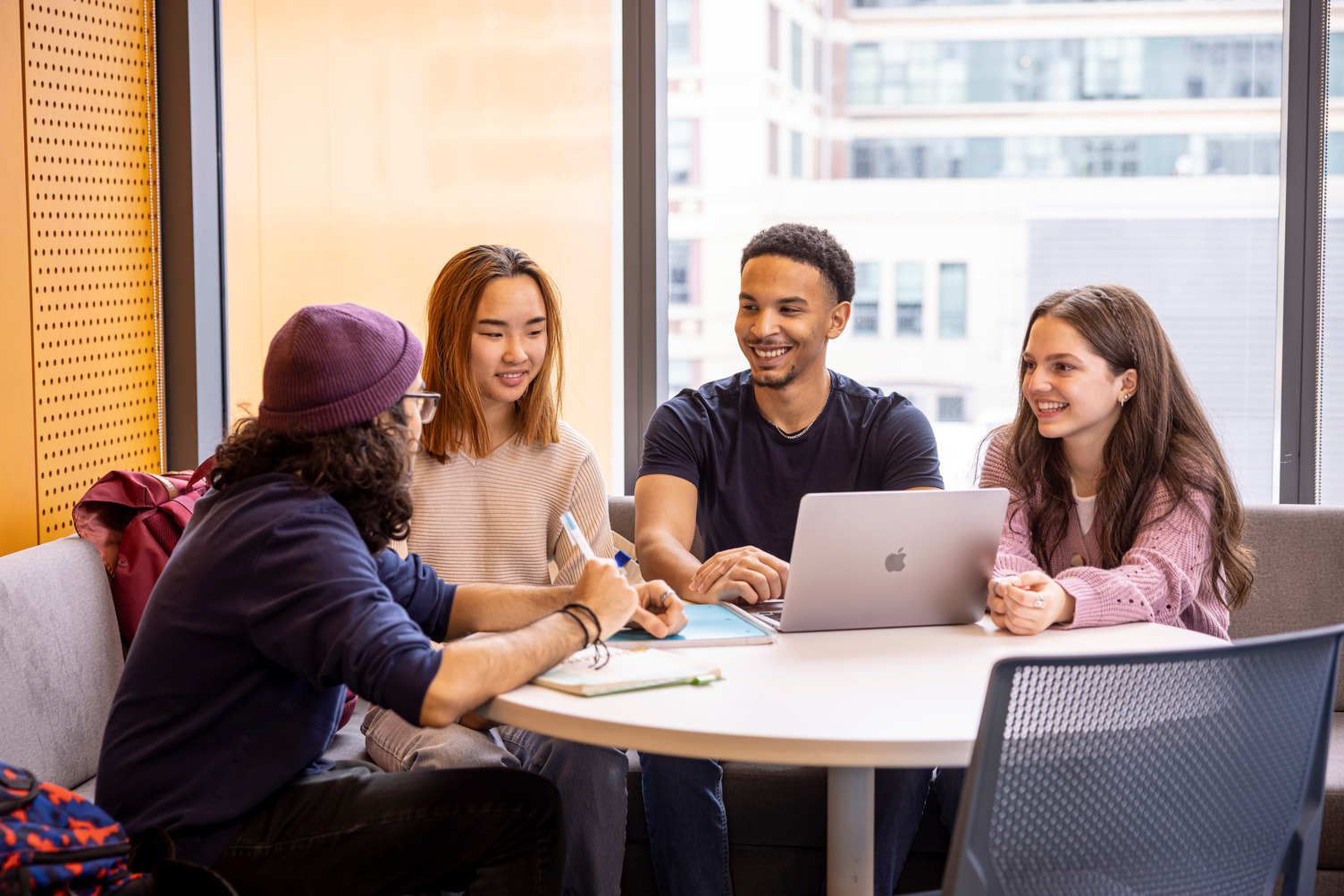 Students sit around a table with a laptop. They are seen talking 