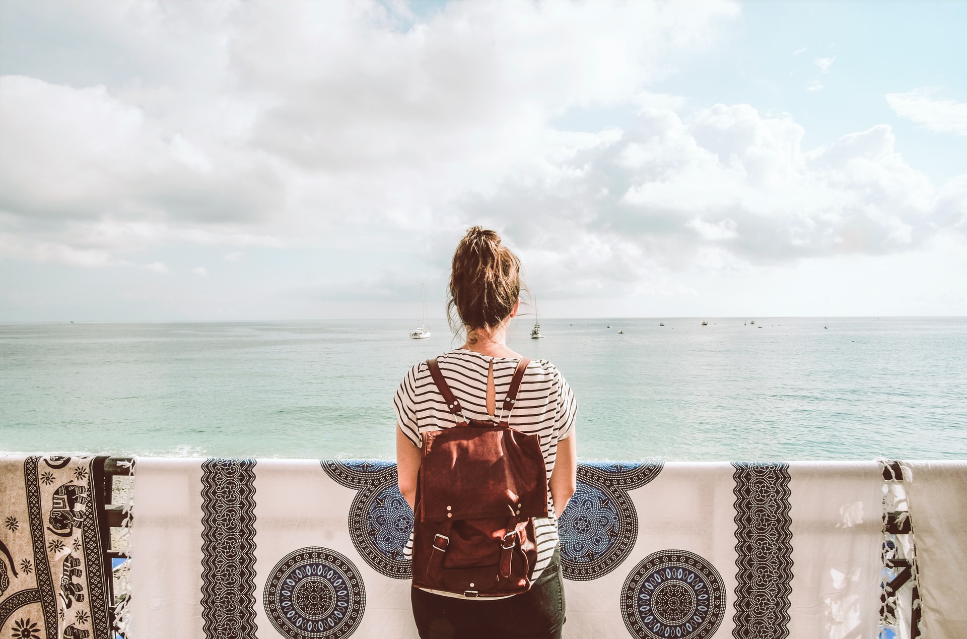 A girl stands in front of a mosque while wearing her backpack.