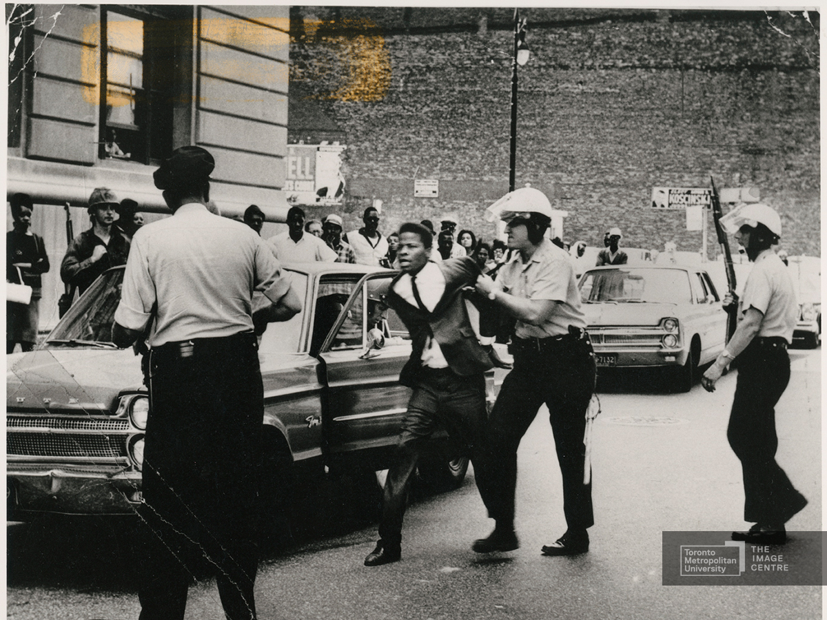 Several policemen arresting a black activist and putting him in a police car.