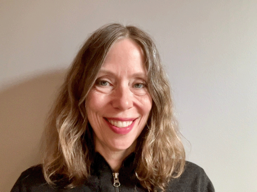 A woman with gray hair smiles while wearing a black sweater.