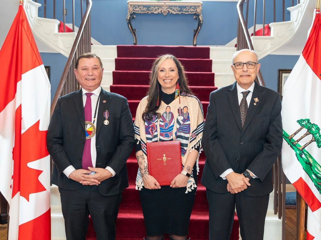 Senator Francis, Pamela Palmater, and His Honour, Dr. Wassim Salamoun. Palmater is holding a red presentation box with the Senate of Canada logo in gold. The Canadian and Prince Edward Island flags are on either side of the group.