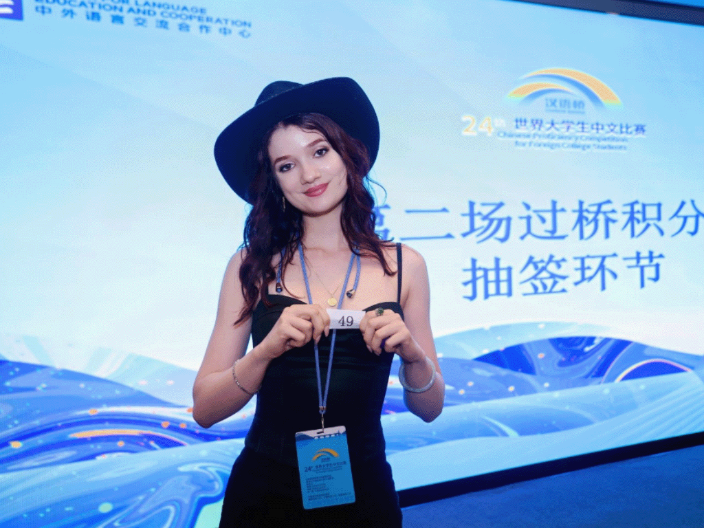 Young woman in a black dress and hat holds a card marked 49 while smiling, set against a blue backdrop with Chinese and English text.