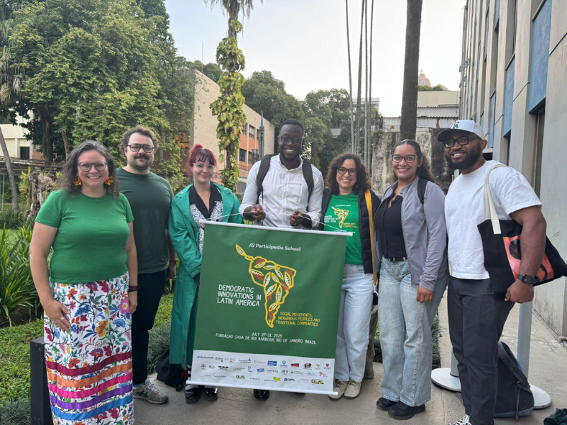 Three people smile in front of a Democratic Innovations in Latin America poster.