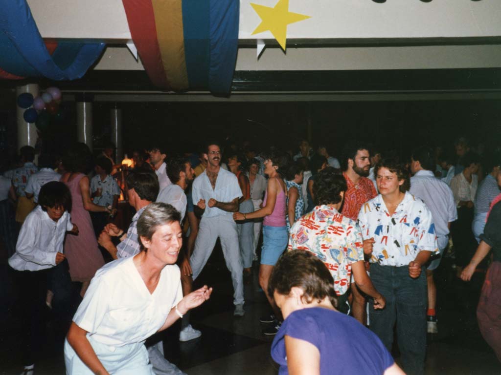 Group dancing in colourful 1980s shirts and banners from the ceiling.