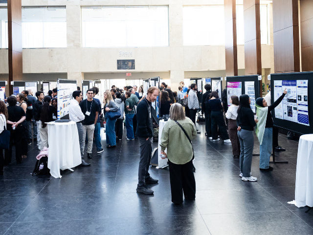 People engaged at a bustling poster presentation event in a bright, spacious hall. 
