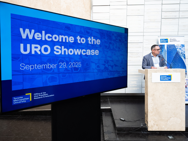 A speaker stands at a podium near a screen that reads Welcome to the URO Showcase.