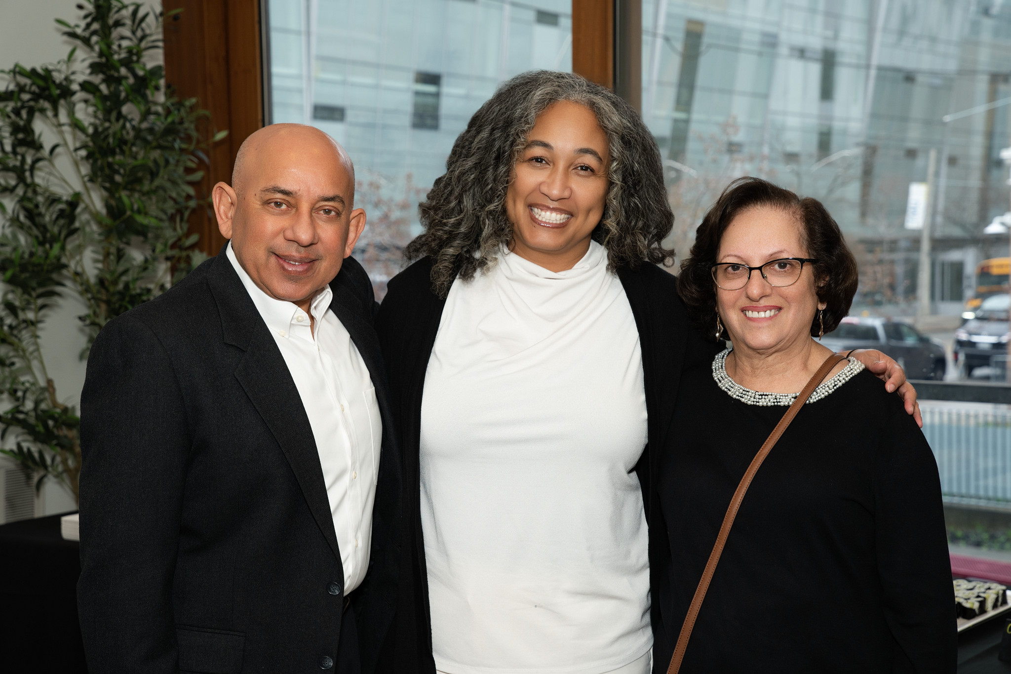 A group of 3 individuals are smiling at the camera and posed together in a straight line. They are all in formal attire wearing white and black.