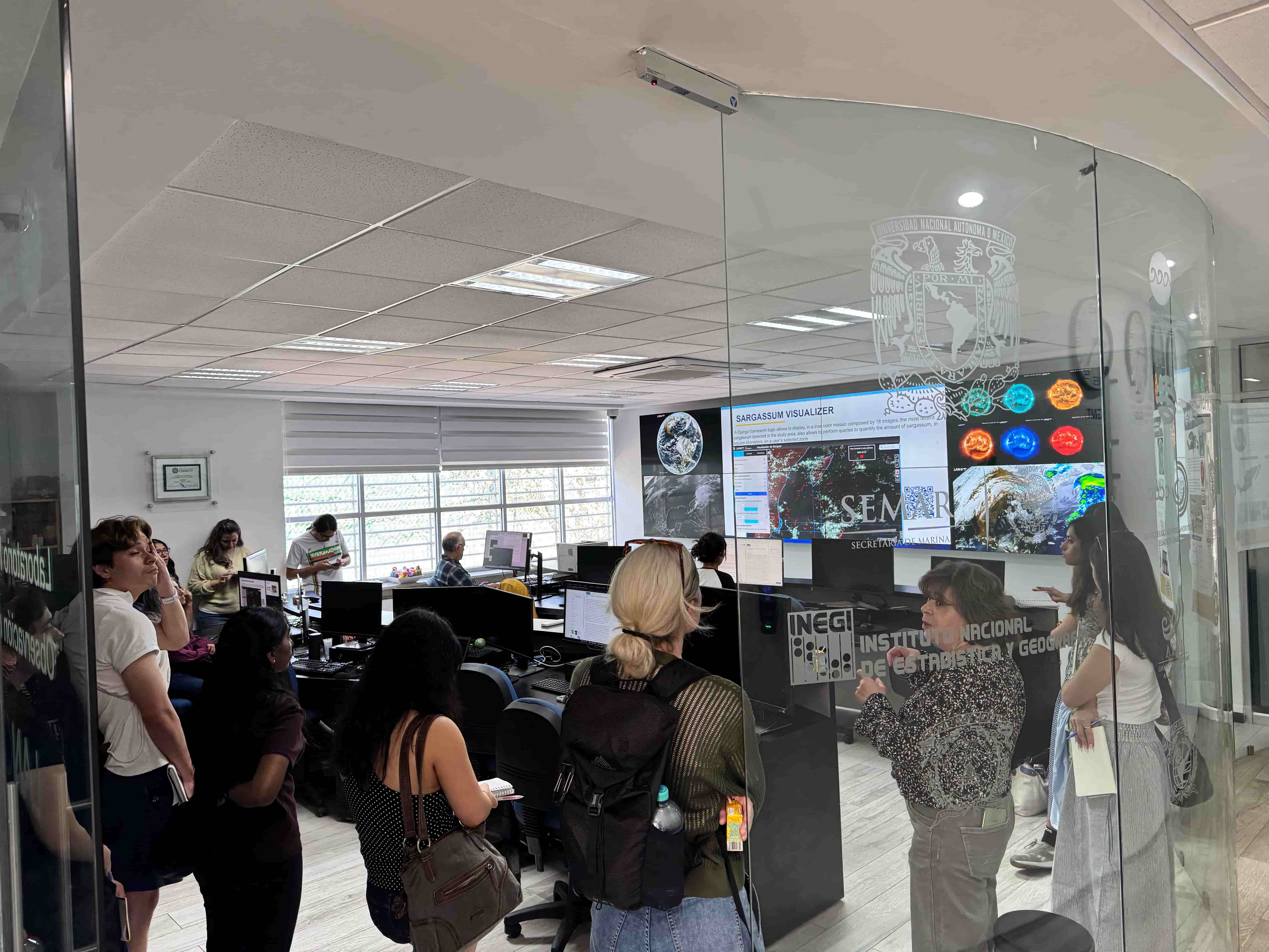 Students are huddled inside a glass room with multiple large screens, displaying different facets of the data collection. 