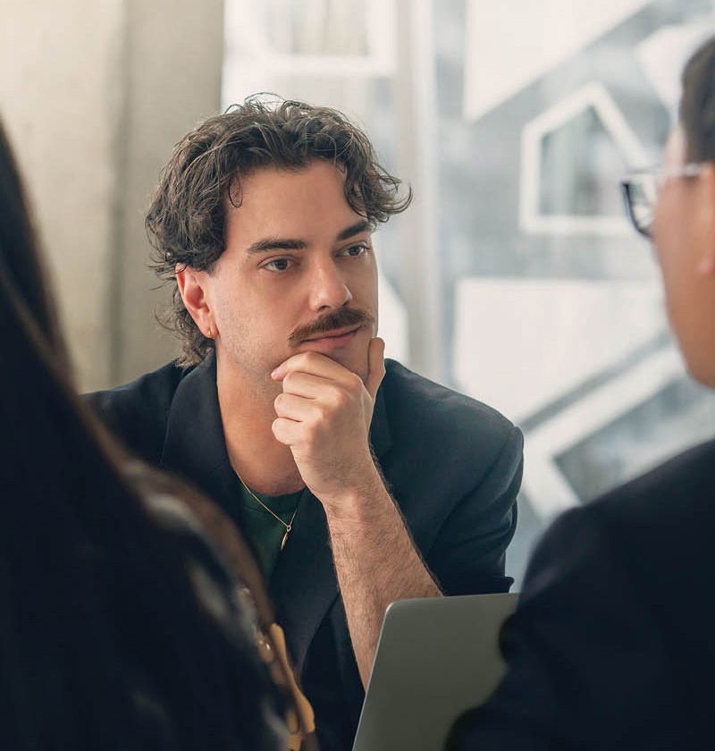 A man with a mustache in a blazer looks thoughtful.
