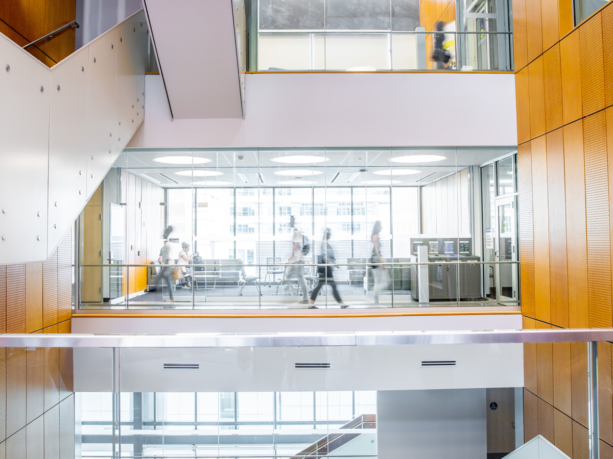 People walking through a bright modern office building with glass walls and wooden panel accents.