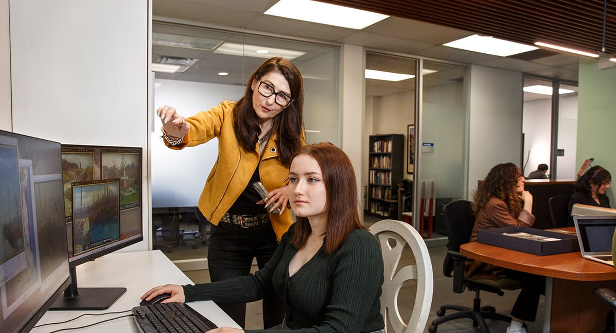 Two females looking at a dual screen computer, engaged in discussion