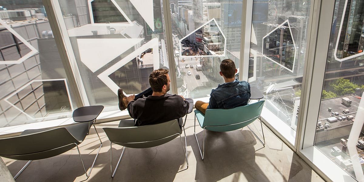 Two male students sitting on chairs looking at a view from a top rise building