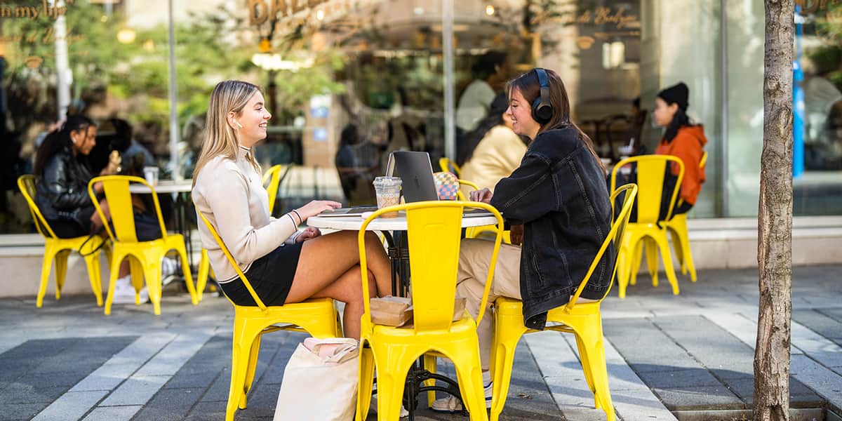 Two female students sitting on yellow chairs in front of each other chatting.