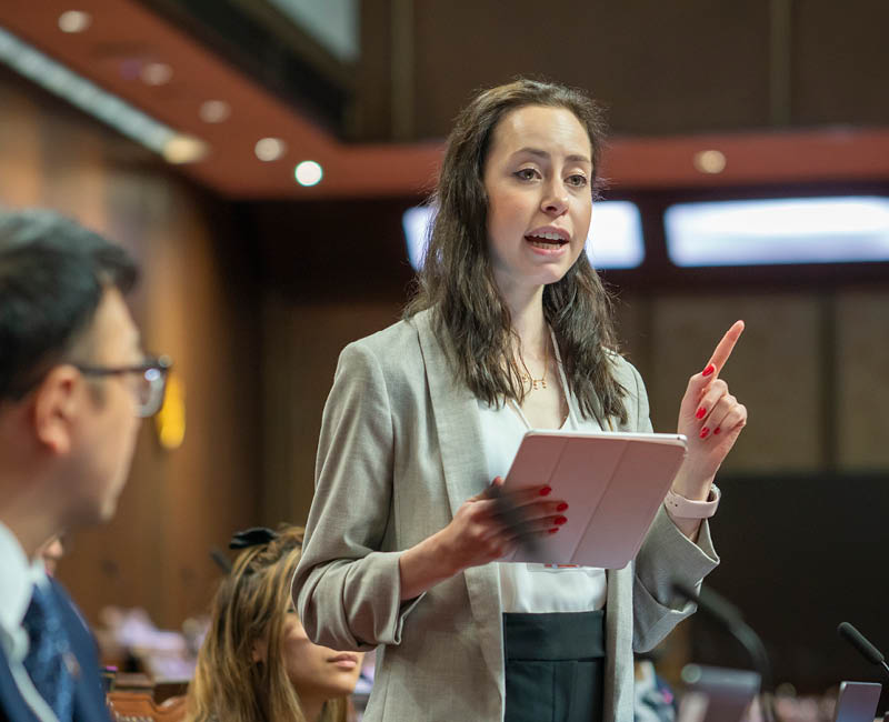 A woman talking in assembly with a pink ipad in her hand as others listen carefully