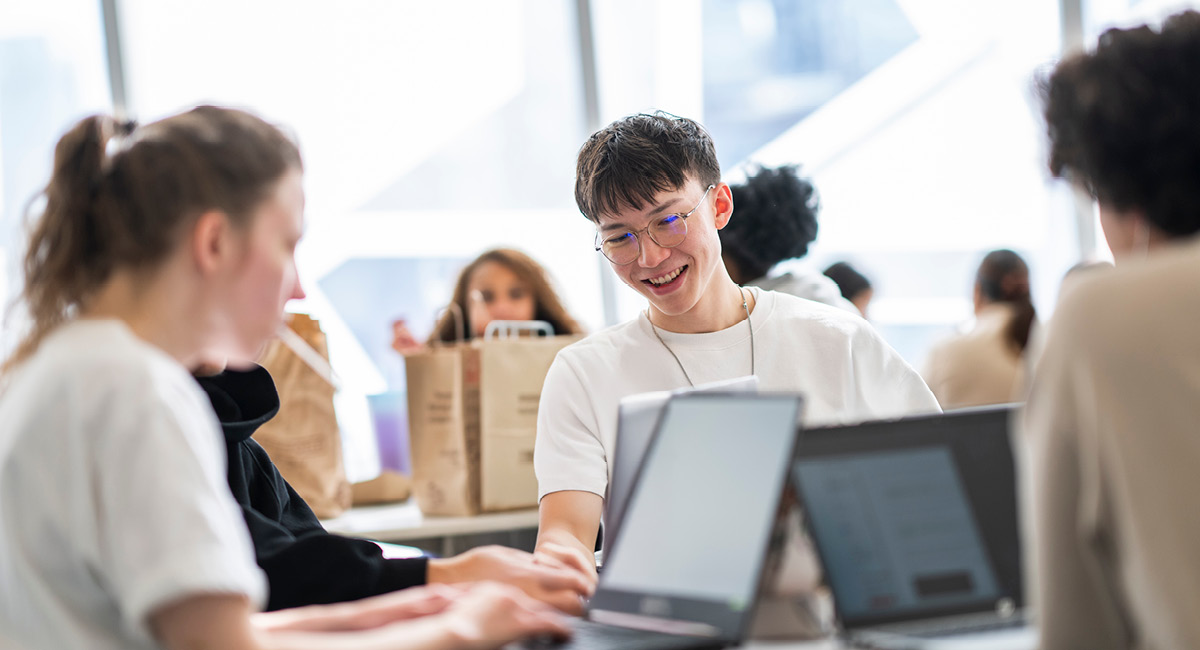 Group gathered around laptops in bright room; one person smiles, creating a friendly, collaborative atmosphere.