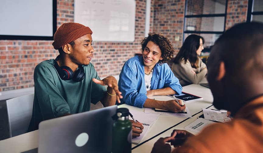 A diverse group of four people discuss around a table in a modern office, collaboratively.