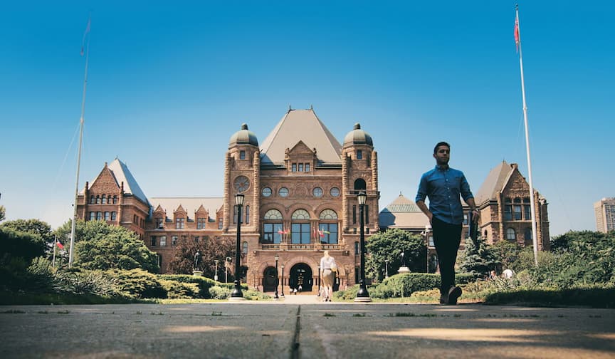 A person walks on a path by Queen's Park under a clear blue sky.