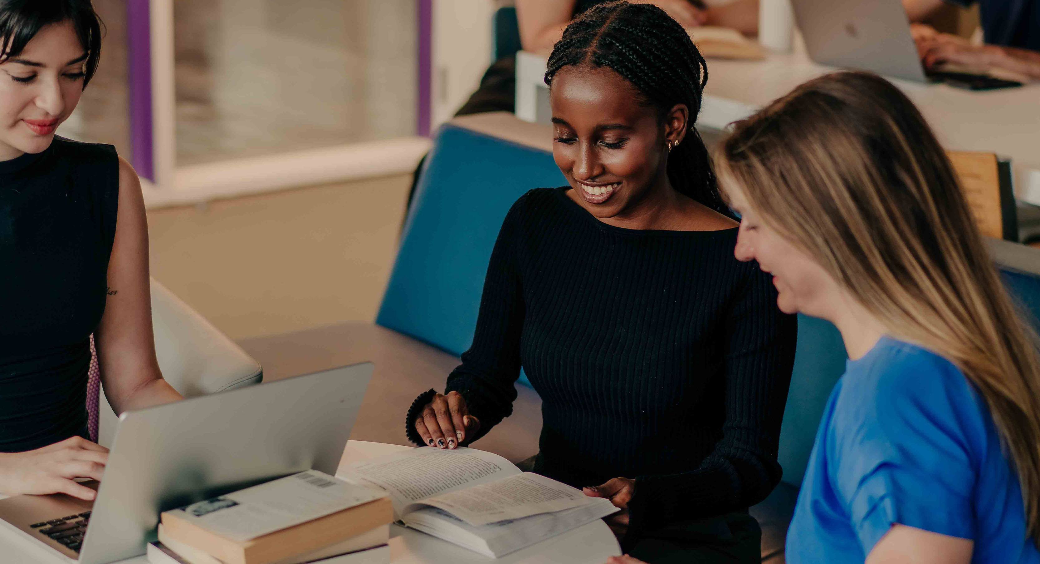 Three students studying and smiling with laptops and books.
