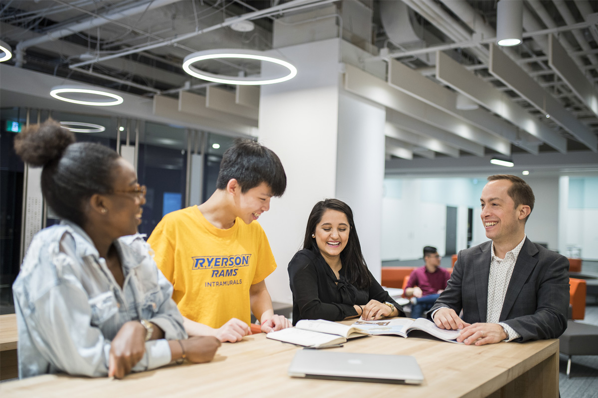 Three students smiling and conversing with a professor