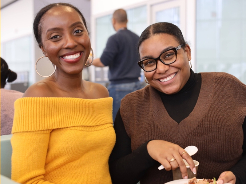 Two Black staff members posing for a photo while seated