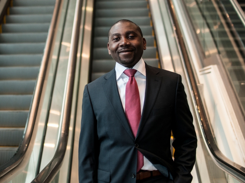 Black graduate student wears a suit and poses at the bottom of escalator