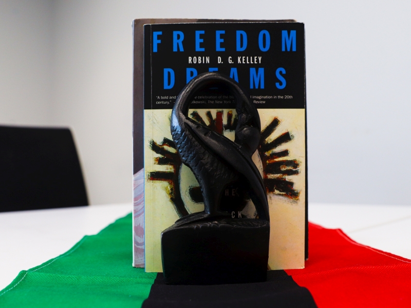 Statuette of a sankofa in front of the Freedom Dreams book resting on a pan-African flag in a decorative montage
