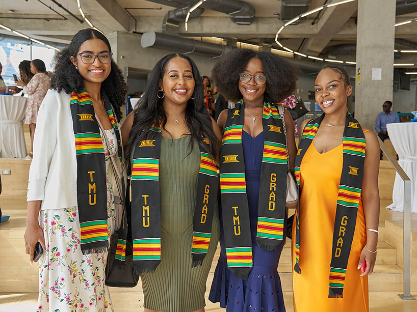 Four graduates smiling and wearing Black excellence Kente stoles