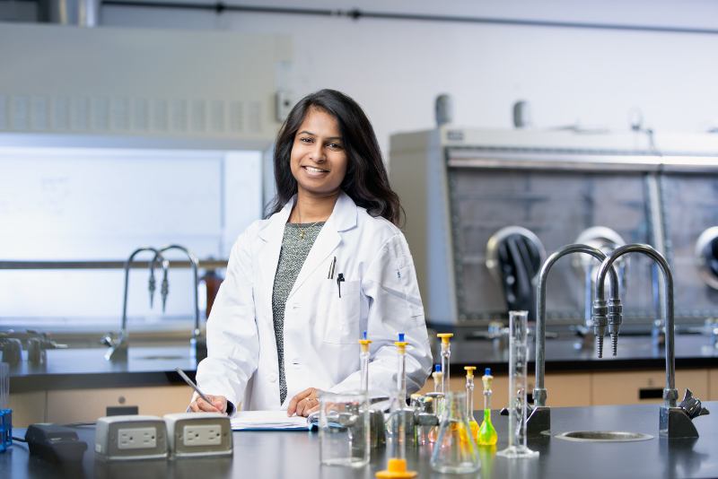 A woman stands in a lab wearing a white lab coat