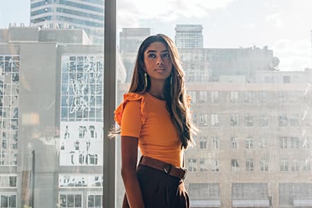 Student standing indoors with large windows behind her showing a city skyline