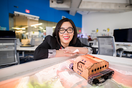 Student smiling while working on a detailed architectural model in a lab setting.