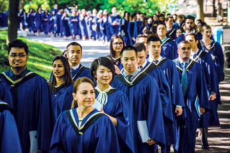 Large group of graduates in blue convocation gowns walking together outdoors.