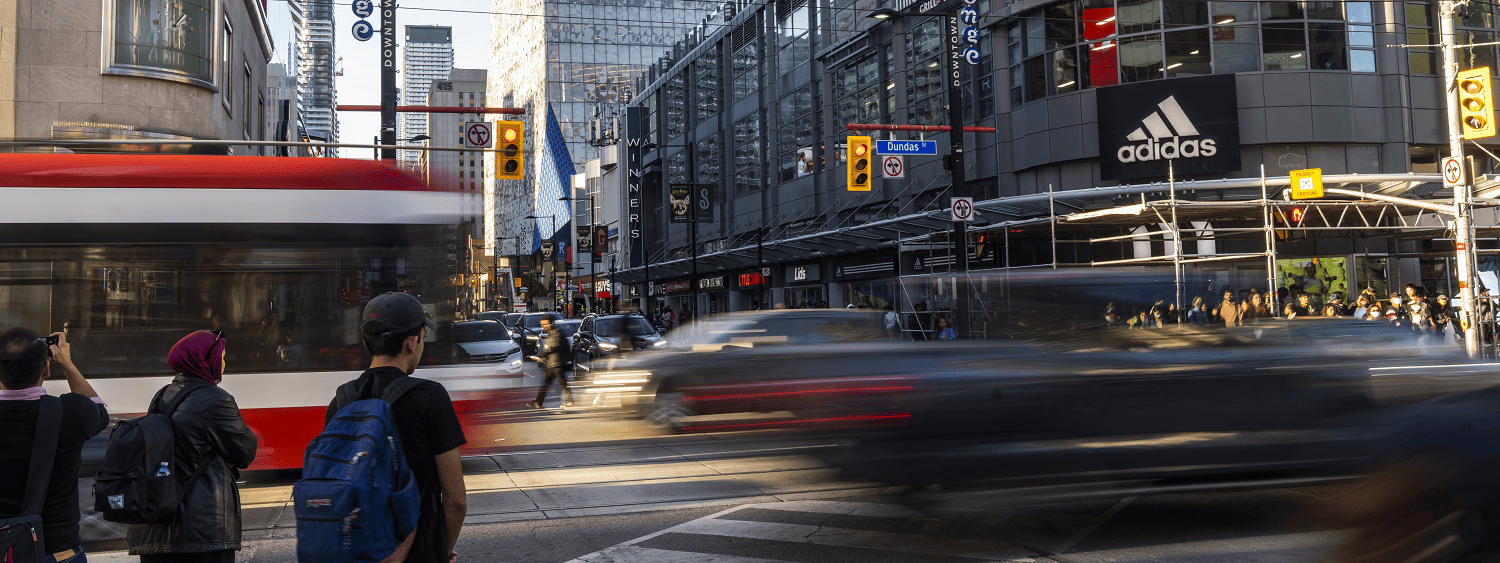 Busy crossing at Yonge and Dundas square with people, buildings, cars and a bus in the background
