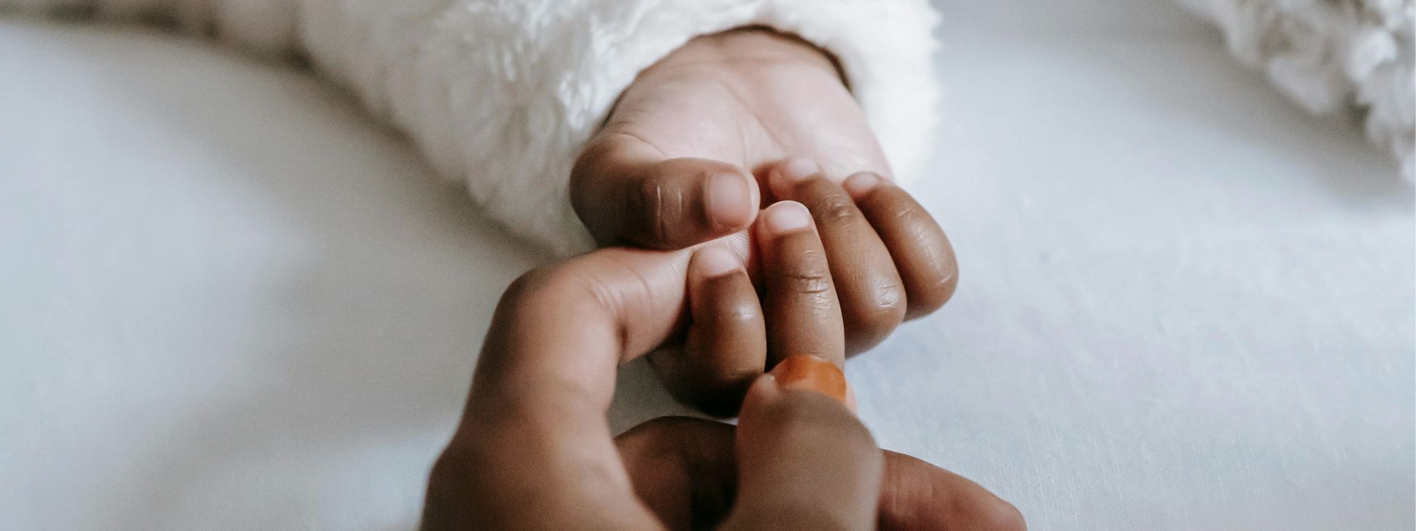 A baby's hand wrapped around a mother's finger