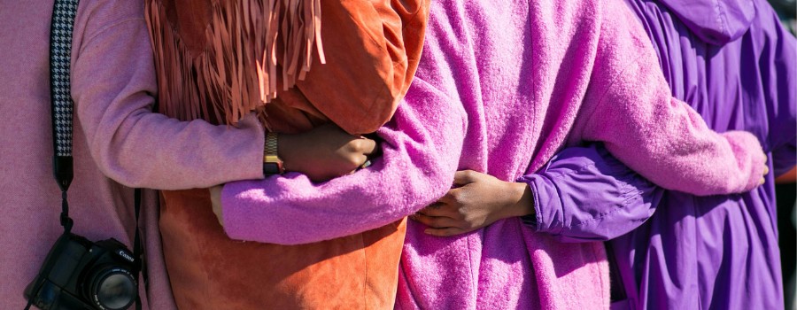 Four women hugging each others at the waist, pictured from the back