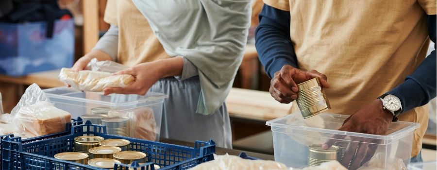 Two individuals, a mand and a woman, filling up a donation box with food