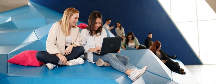 Two students are studying with a laptop in Sandbox by DMZ in SLC. Other students can be seen in the background.