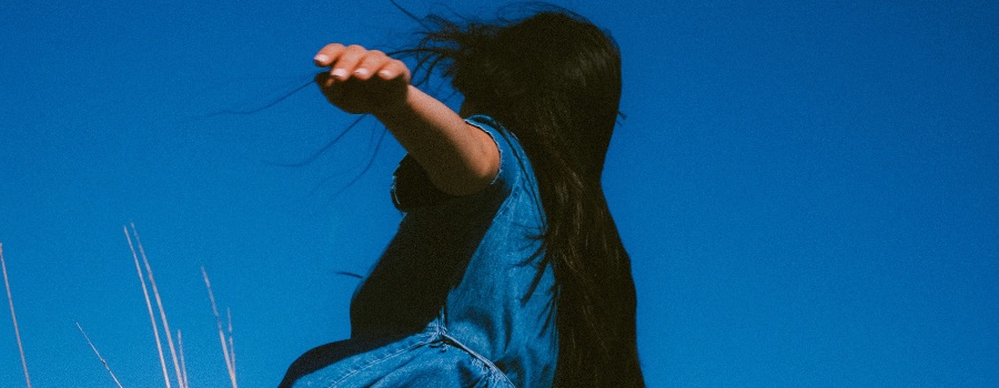 A young girl with her arm raised in a field, blue sky behind her